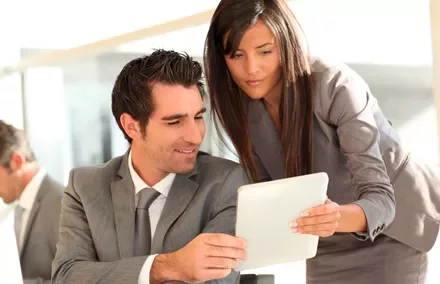 Dos personas en trajes formales revisando una tableta en una oficina.
