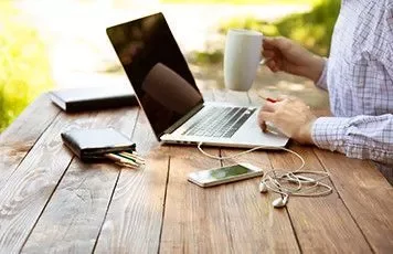Persona utilizando una laptop sobre una mesa de madera al aire libre.